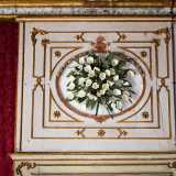Grossi specchi dalle cornici in oro si alternano a riquadri con ghirlande di fiori bianchi aggettanti
